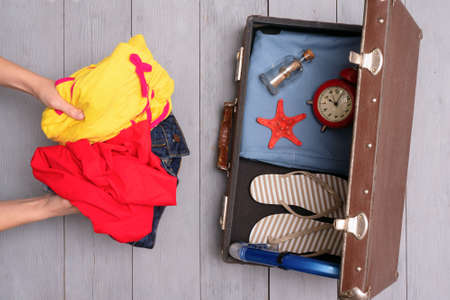 Female hand and old retro suitcase with clothing on the wooden floor background. Top view.の写真素材