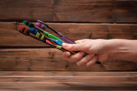 Heap of toothbrushes in female hand close up on brown wooden background.の写真素材