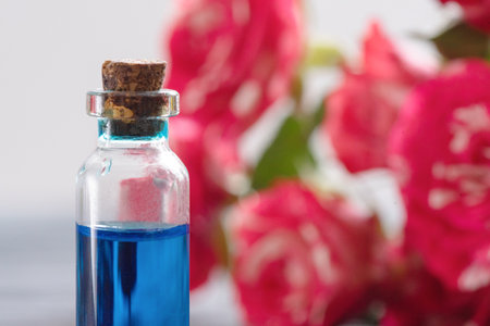Blue liquid in the bottle on the red roses background close up.の写真素材