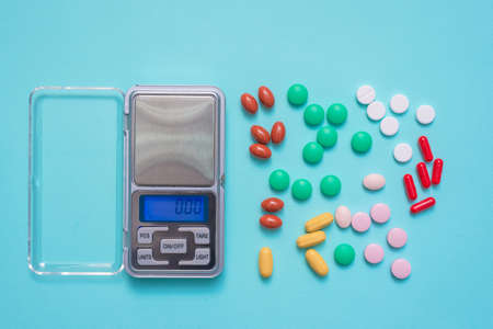 Medical pills assortment and digital weights on the blue background.