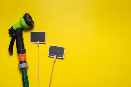 Garden sprinkler and wooden small plant nameplates on the yellow flat lay background with copy...