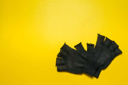 Pair of black construction gloves isolated on the yellow background.