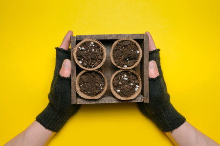Flower pots with a garden soil with a fertilizer in the gardener hands on a yellow flat lay background. Gardening.の写真素材