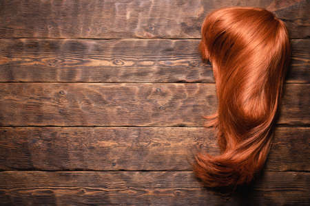 Women redhead long hair wig on the wooden flat lay background.
