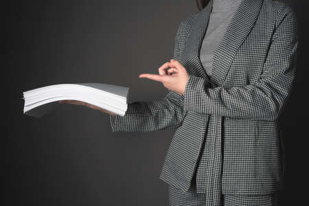 Woman a secretary is showing by her index finger on the heap of documents in her hands.