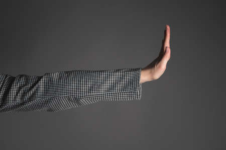 Women hand is showing a stop gesture close up on the gray background.