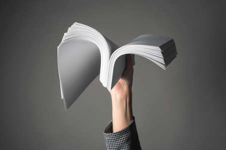 A heap of documents in female hand above the head close up on the gray background.の写真素材