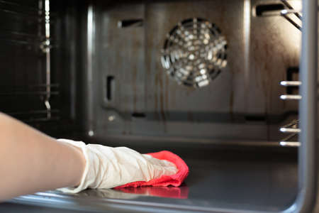 Woman is washing a kitchen gas stove by the rag with detergent close up.