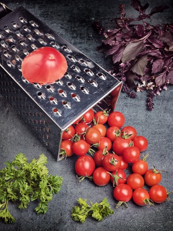 Culinary concept. Still life. Kitchen accessory. Preparation recipe tomato juice. Large tomato and old grater down to small grape cherry tomatoes on retro vintage rustic gray stone background. Low calorie food.の写真素材