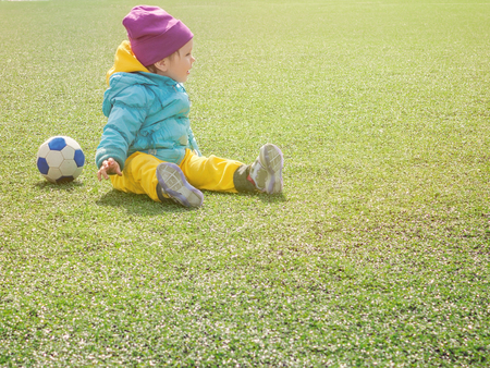 Little girl child on football field, in sportswear, training, plays with soccerball on artificial lawnの写真素材