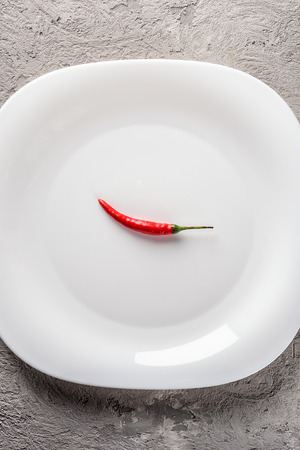 One red chili pepper on white plateの写真素材