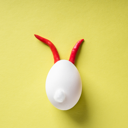 Egg shell and red hot chilli pepper imitation rabbit hare face of devil clown on yellow colored background paper. Food concept minimal Easter Halloweenの写真素材