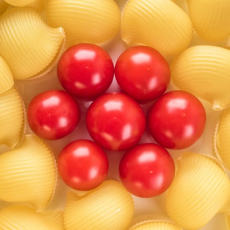 Food background Uncooked Macaroni Lumaconi close-up macro red Cherry Tomatoes in flower form Concept...