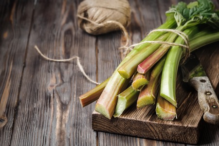 Stems of fresh young rhubarb with kitchen knife on cutting board Ingredients for food recipes healthy diet detox organic food vegetables on wooden background, low key copy space top view soft focusの写真素材