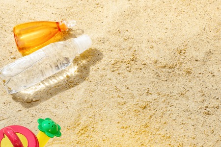 Beach Summer Sun Sand Kids Toys and bottle water slippers and Sunscreen concept of childrens leisure tourism entertainment games Skin Protection SPF UVA UVB radiation safety from Melanoma Cancer.の写真素材