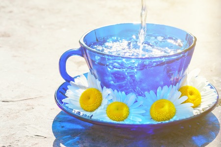 Drink beverage from chamomile herbs in tea blue glass cup on village table outdoor sunny hot afternoon hard sunlight with copy space.の写真素材