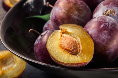 Whole fresh ripe red violet blue plums and slices cut in bowl on kitchen table Concept of cooking jam compote homemade do by one's own hands harvest of agriculture top view with copy space.の写真素材