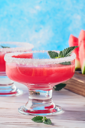 Drink smoothies from red watermelon in glass dishes decorated white sugar and mint leaves Pieces of fruit on cutting board white table and blue background concept of healthy eating diet detox.の写真素材