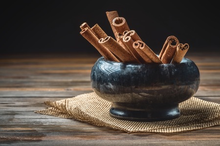 Cinnamon sticks in marble bowl on a wooden table. Dark rustic style baking concept with copy spaceの写真素材