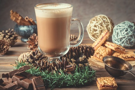 Glass cocoa mug or coffee with milk froth on wooden table served cookies cinnamon chocolate and...