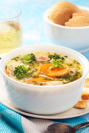 Italian vegetable soup with broccoli carrots noodles in chicken broth on blue table with slices of bread and glass juice. Food vegetarian organic still life in light style close-upの写真素材
