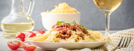 Italian pasta bolognese penne rigatone minced meat in tomato sauce and parmesan cheese. Still life on white wooden table served with cherry tomatoes, carafe of olive oil and glass of white wineの写真素材