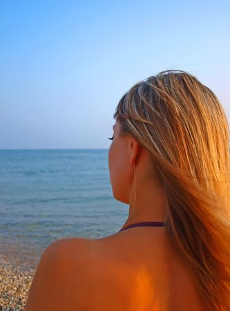 Young woman staring at the sea and thinking of something at the golden sunset      の写真素材