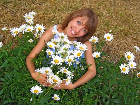 Blonde smiling girl with a lot of camomiles in her handsの写真素材