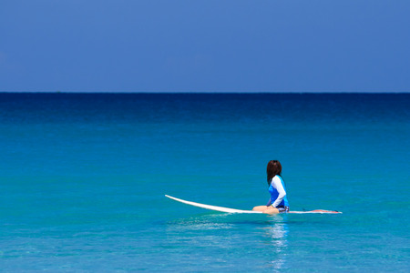 Surfer girl sitting on surfboard in water at the beach. Kata Beach, Phuket, Thailand.の写真素材