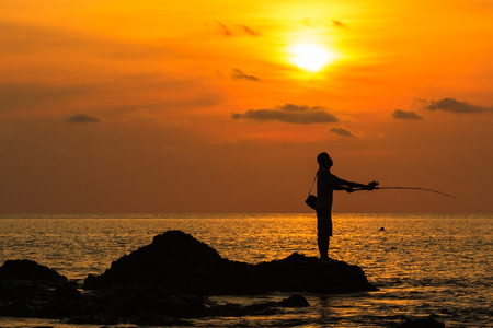 Silhouette of man fishing on the beach at sunset.の写真素材