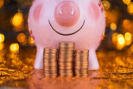 stack of coins and pink piggy bank with yellow blurred bokeh background.の写真素材