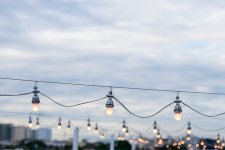 Light bulbs on string wire against cloud and sky background.の写真素材
