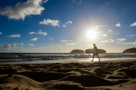 Silhouette of man is walking on the beach with a surfboard in his hands.の写真素材