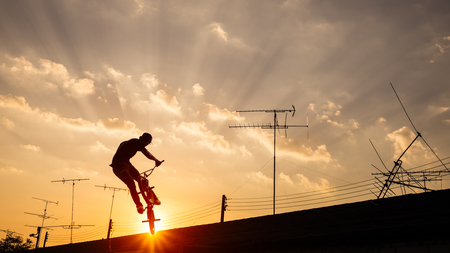 Silhouette of a man  jumping on bmx bike on roof of the house against sky at sunset.の写真素材