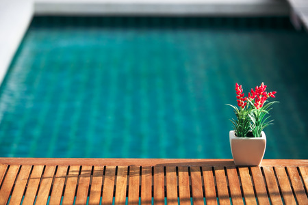 Red decoration artificial flower on wooden table with swimming pool background.の写真素材