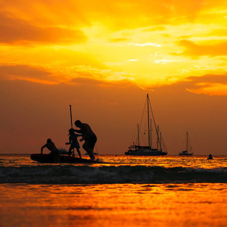 Silhouettes of group of people in ocean at sunset, Nai Harn beach, Phuket, Thailand.の写真素材