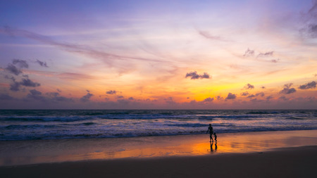 Silhouette of mother and child holding hands in sunset at the beach.の写真素材