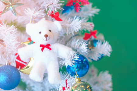 White teddy bear and christmas tree decorated with balls and bows on green background. Pastel color.の写真素材