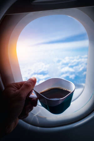 A man drinking a cup of a black coffee in front of airplane window during the flight.の写真素材