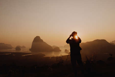 Young man taking picture of sun rise at Samed Nang Chee mountain view point, Phang Nga Province, Thailand.の写真素材