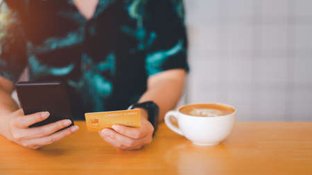 Woman are holding credit card and using mobile phone to pay for online shopping in a coffee shop. Online payment Concept.の写真素材