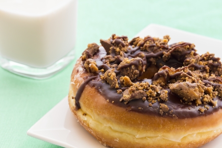 Peanut butter and chocolate covered glazed doughnut with a glass of milkの写真素材