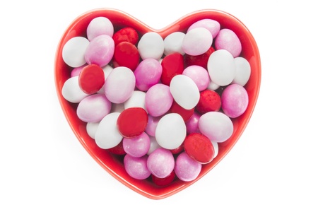 Heart shaped dish full of candy-coated chocolates isolated on white
