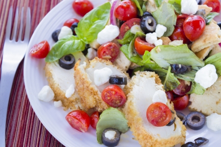 Salad with pita bread, cherry tomatoes, basil, red onion and kalamata olives served with breaded chicken and feta cheeseの写真素材
