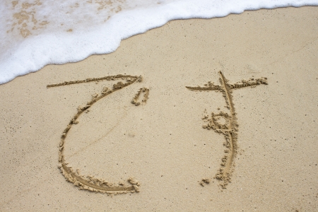 The Japanese word desu (to be) written in sand at water's edgeの写真素材