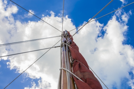 View up a mast of a sailboat against a blue sky with clouds