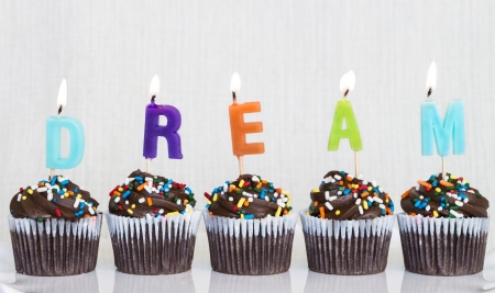 Lit multicolored candles that spell DREAM in chocolate mini cupcakes with colored sprinklesの写真素材