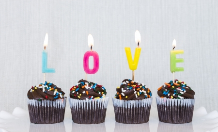 Lit multicolored candles that spell LOVE in chocolate mini cupcakes with colored sprinklesの写真素材