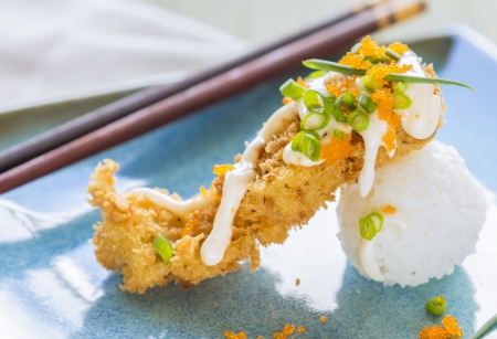 Fried breaded ahi tuna resting on a ball of rice, drizzled with masago mayonnaise, and sprinkled with green onions and masago, also known as capelin fish roeの写真素材