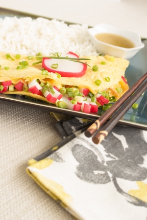 An omelet stuffed with strips of kamaboko, a japanese white fish cake, green onions and American cheese, served with rice and shoyu butter sauceの写真素材